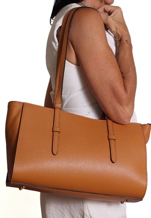 Donna che indossa una canotta bianca senza maniche, con una grande borsa a tracolla in pelle testurizzata color beige sul braccio destro.