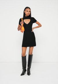 Rochie neagră tricotată cu dungi, cu decolteu decupat, mâneci scurte, asortată cu cizme negre cu toc până la genunchi și o geantă mică portocalie.