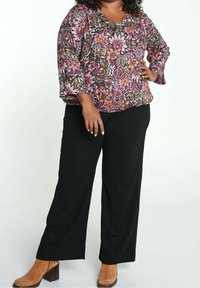 Blouse à motif floral en tons noir, rose et jaune avec un col en V et des manches trois-quarts, assortie à un pantalon noir ample et des bottines marron.