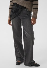 Bredde sorte jeans med en falmet vask, der har et gennemsigtigt sort blondeoverlay ved talje og detaljeret syning langs lommerne.