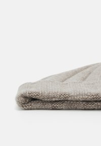 Beige strikket ullhatt med ribbestruktur, brettet nederst. Mykt, tykt materiale med en glatt overflate og subtile mønsterdetaljer.