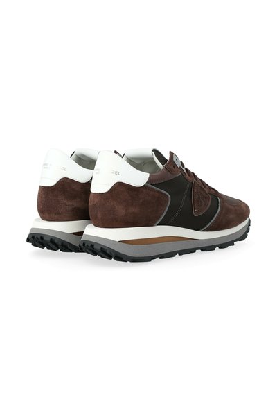 Une paire de baskets en suedine marron et cuir noir avec des languettes blanches au niveau du talon et des semelles en caoutchouc grises, présentée de côté arrière.