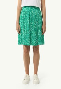 Jupe verte à motif avec taille élastique, longueur genou, dotée d'un design floral avec des accents jaune clair. Assortie à des baskets blanches.
