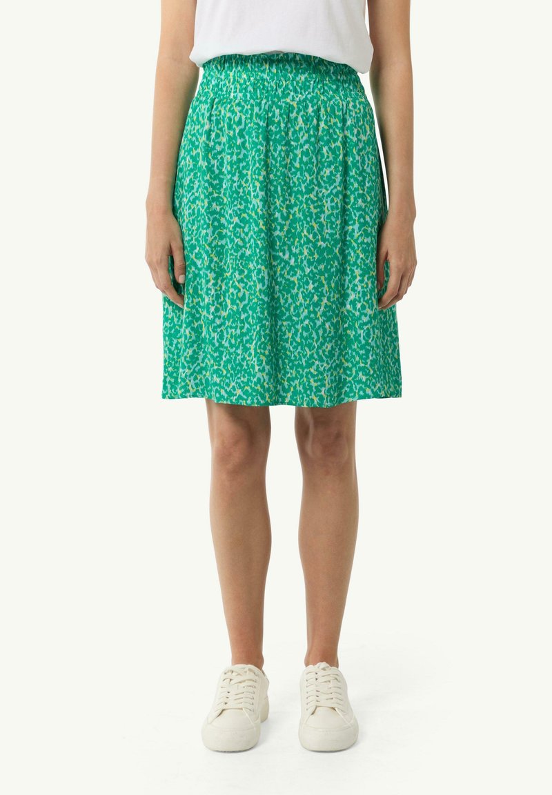 Jupe verte à motif avec taille élastique, longueur genou, dotée d'un design floral avec des accents jaune clair. Assortie à des baskets blanches.