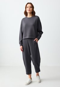 Das graue Sportset umfasst einen verkürzten Pullover mit Rundhalsausschnitt und lockeren Hosen, die seitliche Taschen und einen elastischen Bund haben.