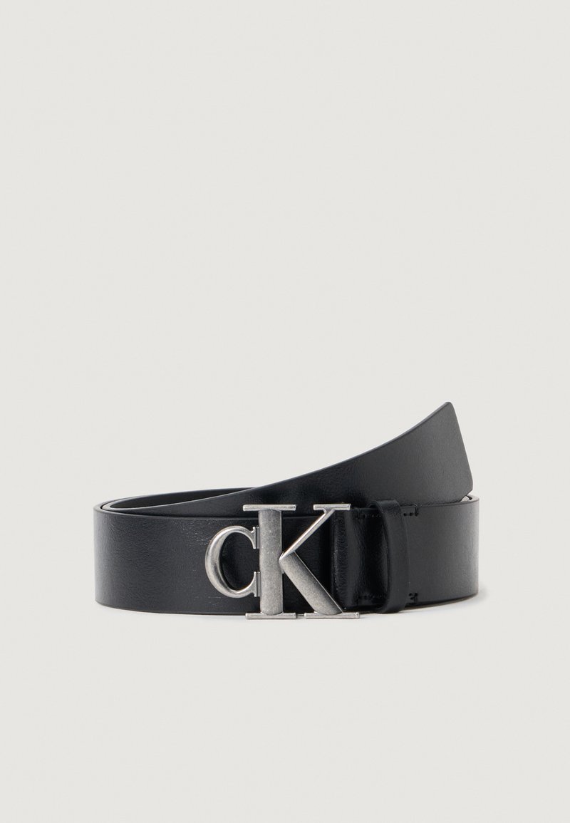 Zwarte leren riem met een gladde textuur, voorzien van een zilveren "CK" metalen gesp. Het design is stijlvol en minimalistich.