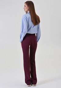 Chemise courte bleu clair associée à un pantalon taille haute bordeaux. La chemise a des manches longues, et le pantalon présente une texture lisse avec un léger évasement.