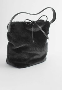 Sac à épaule en fausse fourrure noire avec une bandoulière noire courbée, un haut froncé et un détail en nœud. Texture douce et forme décontractée.