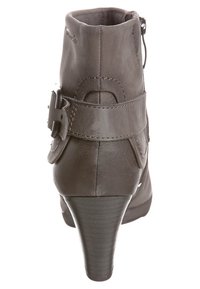 Botín de cuero marrón con tacón alto, que presenta un cierre lateral de cremallera y una correa decorativa con hebilla alrededor del tobillo.