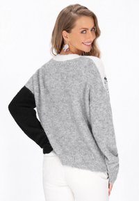 Szary i czarny sweter w kolorowe bloki o luźnym kroju, długich rękawach, zaokrąglonym dekolcie i miękkim, teksturowanym wykończeniu.