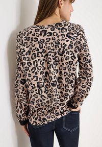 Bluzka z długim rękawem w panterkę, beżowy materiał w czarne plamki, zaokrąglony dekolt, czarne mankiety, luźny krój i przeszycia z tyłu.