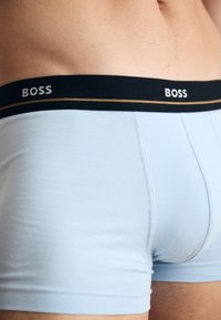 Világoskék boxer alsónemű, puha anyagból készült, fekete derékrésszel, amelyen a "BOSS" felirat és egy arany szegélycsík található.