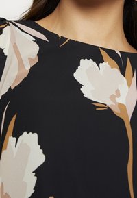 Tessuto nero con grandi motivi floreali bianco, rosa e sabbia. Presenta un collo elegante e arrotondato e una texture liscia.