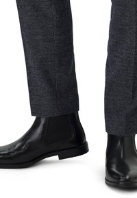 Stivali alla caviglia in pelle nera abbinati a pantaloni scuri con motivo, che mettono in mostra un tessuto testurizzato e una vestibilità su misura con orli puliti.