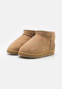 Botines de ante marrón claro con una textura suave, puntera redondeada y suela de goma. Presentan una costura contrastante a lo largo de la parte superior.