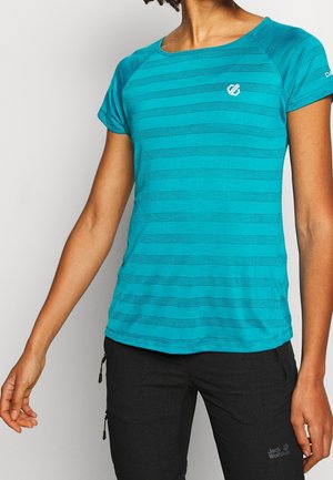 Person iført en kortærmet tealstribet sports-shirt og sorte Jack Wolfskin-bukser, stående med armene afslappet ned langs siderne.