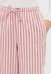 Striped pants in red and white cotton blend, featuring an elastic waistband with drawstring, side pockets, and a loose fit.