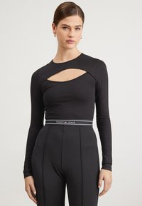 Maglietta nera a maniche lunghe con un design a taglio sul davanti, abbinata a pantaloni a vita alta, accentuati da una cintura elastica con logo.
