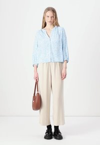 Camicia a bottoni floreale azzurro chiaro con maniche lunghe, abbinata a pantaloni beige a gamba larga e scarpe con plateau nere. Inclusa borsa a spalla marrone.