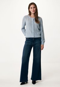 Ljusblå stickad kofta med knappstängning, med vertikal ribbning och öppet stickmönster, i kombination med vida mörka denimjeans.