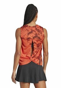 Top deportivo rojo y negro con un patrón texturizado, corte en la espalda y detalle torcido en el dobladillo. Lleva puesto con una falda negra.
