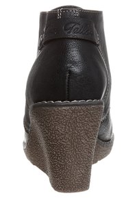 Botte compensée en cuir noir avec une semelle texturée marron, dotée d'un talon incurvé et de coutures à l'arrière.