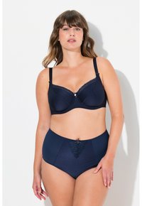 Laivastonsininen rintaliivi, jossa on pilkkukuosi, tukevat langat ja pitsireunus; yhdistettynä korkeavyötäröisiin alushousuihin, joissa on yhteensopivia yksityiskohtia ja pilkkuja.