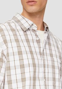 Chemise à boutons en coton blanc avec un motif à carreaux marron et gris. Elle présente un col pointu et une poche poitrine unique.