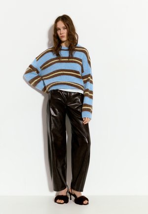 Gestrickter Pullover in blau-braunen Streifen, oversized Passform. Schwarze Leder-Hose mit weitem Bein und braune Fell-Sandalen runden den Look ab.