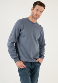 Felpa grigia con colletto girocollo e maniche lunghe, realizzata in tessuto morbido, con colletto e polsini a righe, abbinata a jeans in denim blu.