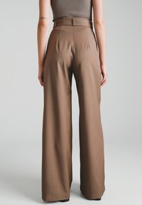 Brązowe spodnie o szerokich nogawkach wykonane z gładkiej, lekko elastycznej tkaniny, z wysokim stanem i czystymi szwami, zaprojektowane na luźny krój.