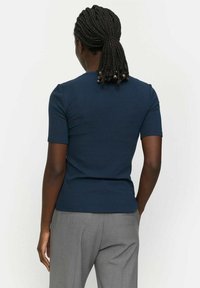 Marineblå ribbet T-shirt med korte ærmer og tætsiddende design. Glat tekstur, rene linjer og en simpel rund halsudskæring, kombineret med grå bukser.