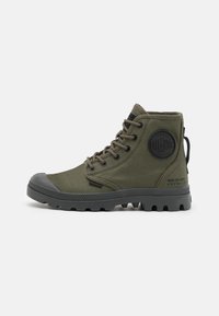 Bottines chevilles vert olive en toile avec une coque de protection en caoutchouc, à lacets, avec une surface texturée et un patch rond de marque sur le côté.