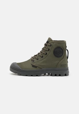 Bottines chevilles vert olive en toile avec une coque de protection en caoutchouc, à lacets, avec une surface texturée et un patch rond de marque sur le côté.