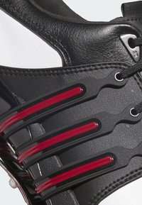 Czarne syntetyczne sneakersy z białymi akcentami, z czerwonymi dekoracyjnymi paskami, teksturowaną powierzchnią i czarnymi sznurówkami. Lekka konstrukcja zapewniająca wygodę.