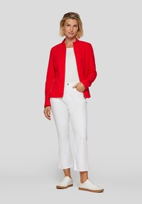 Red zip-up jacket with a ribbed texture, paired with white cropped jeans. The outfit includes white sneakers with beige soles.
