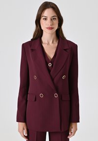 Bordeaux dubbelbreasted blazer met verticale strepen, hardware accenten in goudkleur, en twee voorkudgetasken. Getailleerde pasvorm met gekartelde revers.