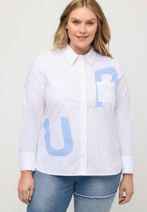 Camicia bianca con maniche lunghe, caratterizzata da lettere stampate di colore azzurro "U" e "P" sul davanti, e una tasca sul petto.