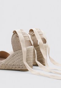 Sandalias de cuña beige con parte superior de yute trenzado y tela, con largas correas de tela para atar. Acentos texturizados en la parte posterior.