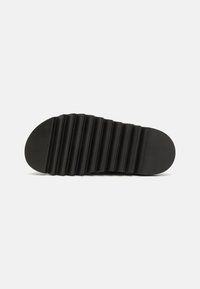 Semelle de chaussure en caoutchouc noir avec un motif texturé et rainuré, et un bout rond. Le dessous est plat, ce qui améliore l'adhérence et la stabilité.