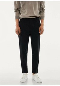 Pantaloni neri sartoriali con un taglio dritto, realizzati in un tessuto liscio, abbinati a scarpe da ginnastica bianche. Il maglione presenta maniche arrotolate.