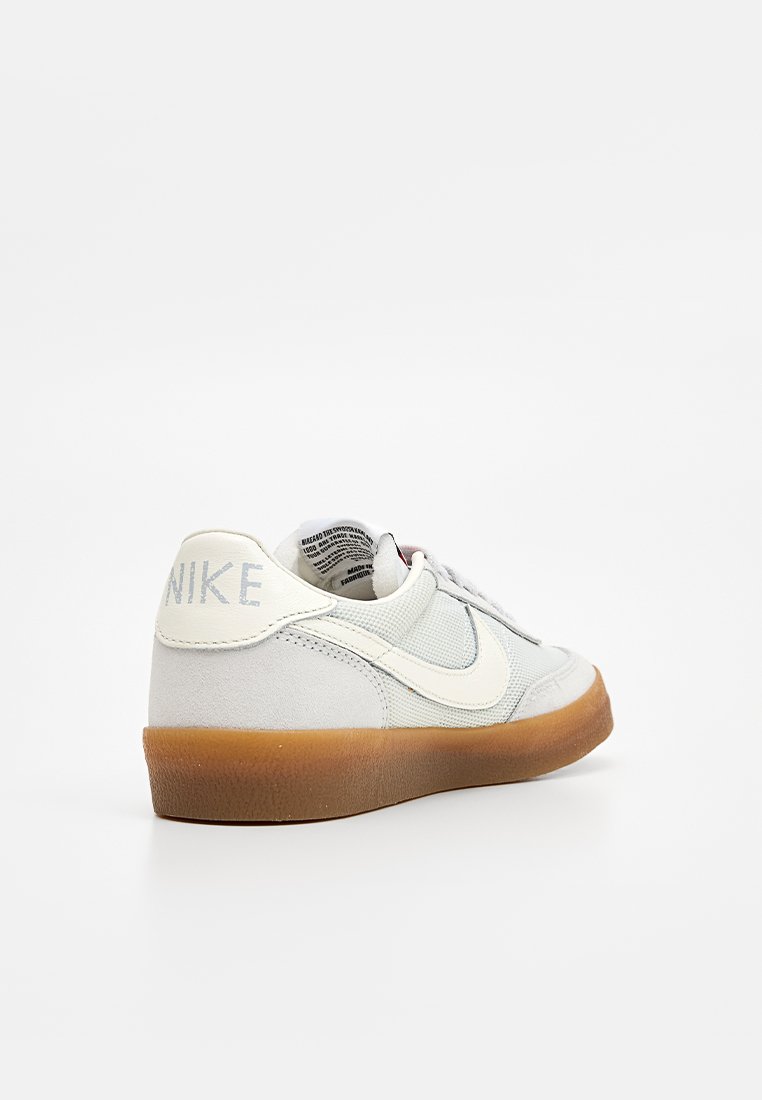 Zapatillas Nike con una parte superior de ante y malla en gris claro, detalles en blanco roto y suela de goma con textura suave.