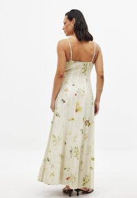Maxi šaty bez rukávov s kvetinovým vzorom v svetlo béžovej farbe, ktoré majú výrazné botanické motívy a voľný strih s bočnými rozparkami.