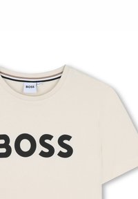 Beige cotton t-shirt with a round neckline and short sleeves, featuring bold black "BOSS" lettering across the front.