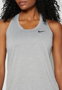 Grå Nike-linne med rund halsringning och en subtil logotyp. Tyget verkar mjukt och något texturerat, lämpligt för sportkläder.