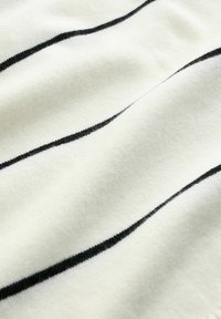 Tissu blanc à rayures horizontales noires. Texture douce, légèrement froissé, avec des fibres visibles créant une apparence chaleureuse.