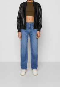 Svart konstläder bomberjacka, olivgrön crop top, högmidjade blå jeans och vita sneakers; avslappnad stil med en ledig silhuett.
