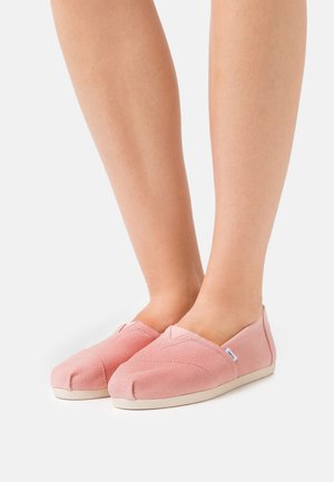 Pink canvas slip-on shoes with a rounded toe, textured upper, side stitch detailing, and a white rubber sole.