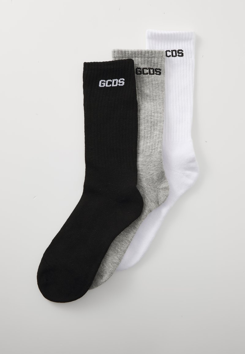 Trois paires de chaussettes en coton côtelé noires, grises et blanches, avec le logo brodé "GCDS" près du haut. Hauteur standard de type crew.
