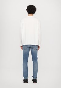 Hvit langermet skjorte med en avslappet passform, kombinert med blå skinny jeans og svarte joggesko. Skjorten har rund hals.